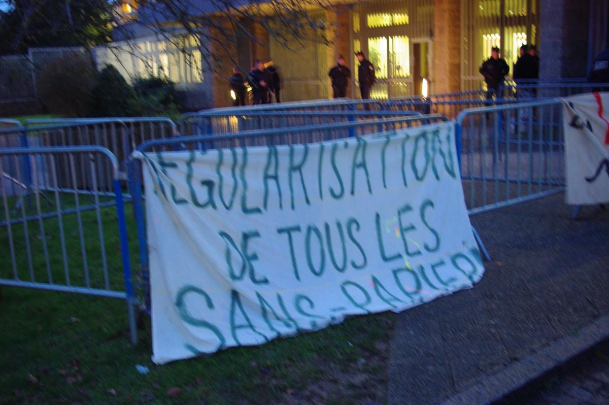 banderoel pour la rgularisation des sans papiers sur les barrières protégeant la préfecture et policiers en arrière plan