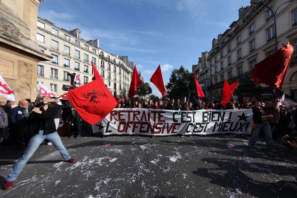 Manifestante avec un drapeau rouge devant la banderole de la CGT spectacle et de Jolie Mome : La retraite c'est bien l'offensive c'est mieux
