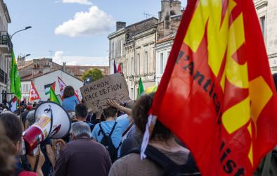 Manifestant tenant une pancarte "Macron face de fion". Un drapeau NPA est tenu par un autre manifestant lors de la manifestation contre le coup de force de macron.