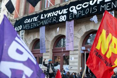 Banderole Gaité lyrique 400 vies en danger, 80 emplois menacés, deux drapeaux NPA sur les côtés flou gaussien, un homme poings brandis au centre 