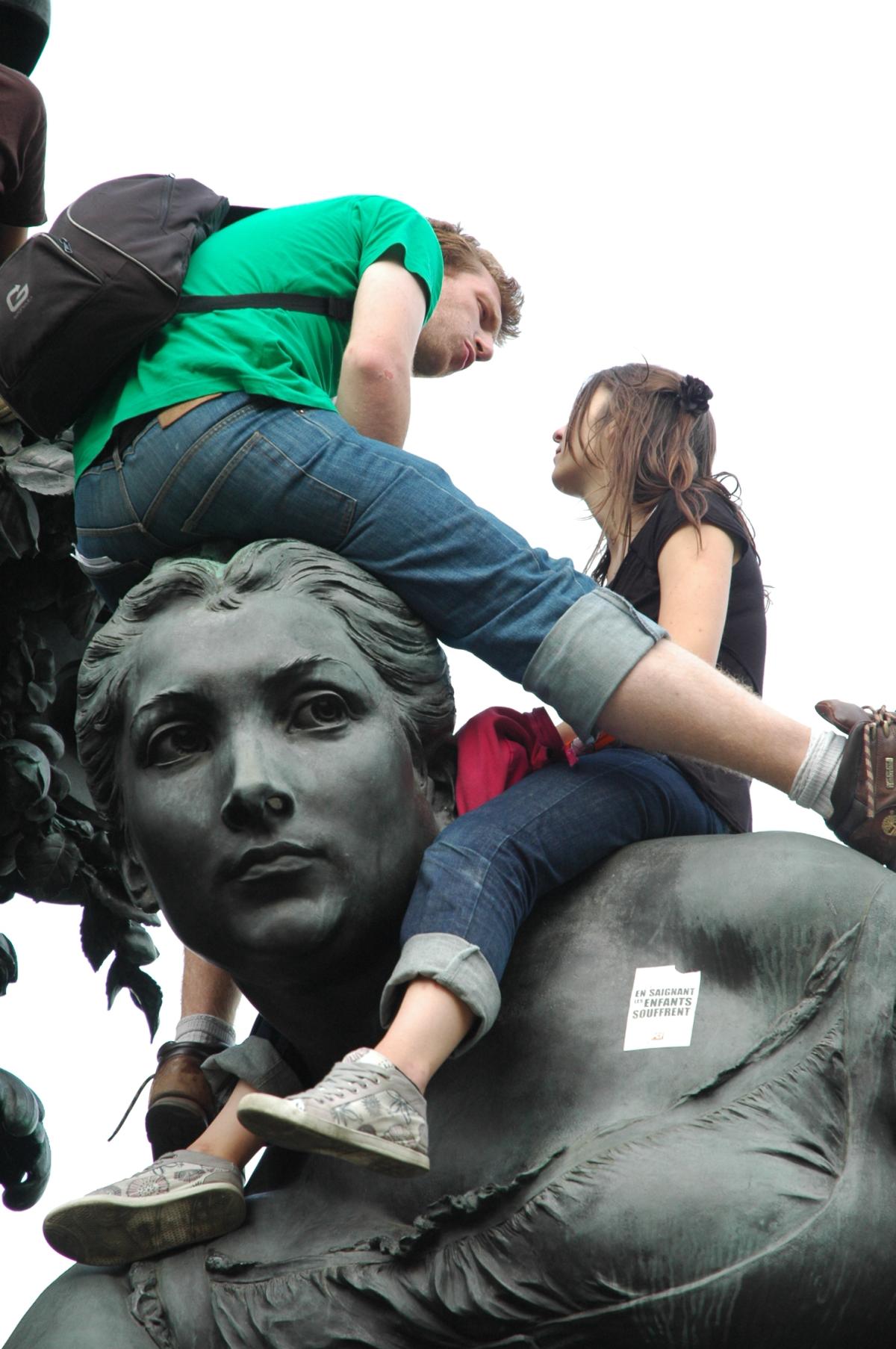 Couple de jeunes manifestants assis sur tête de statue de la place de la nation à Paris.
