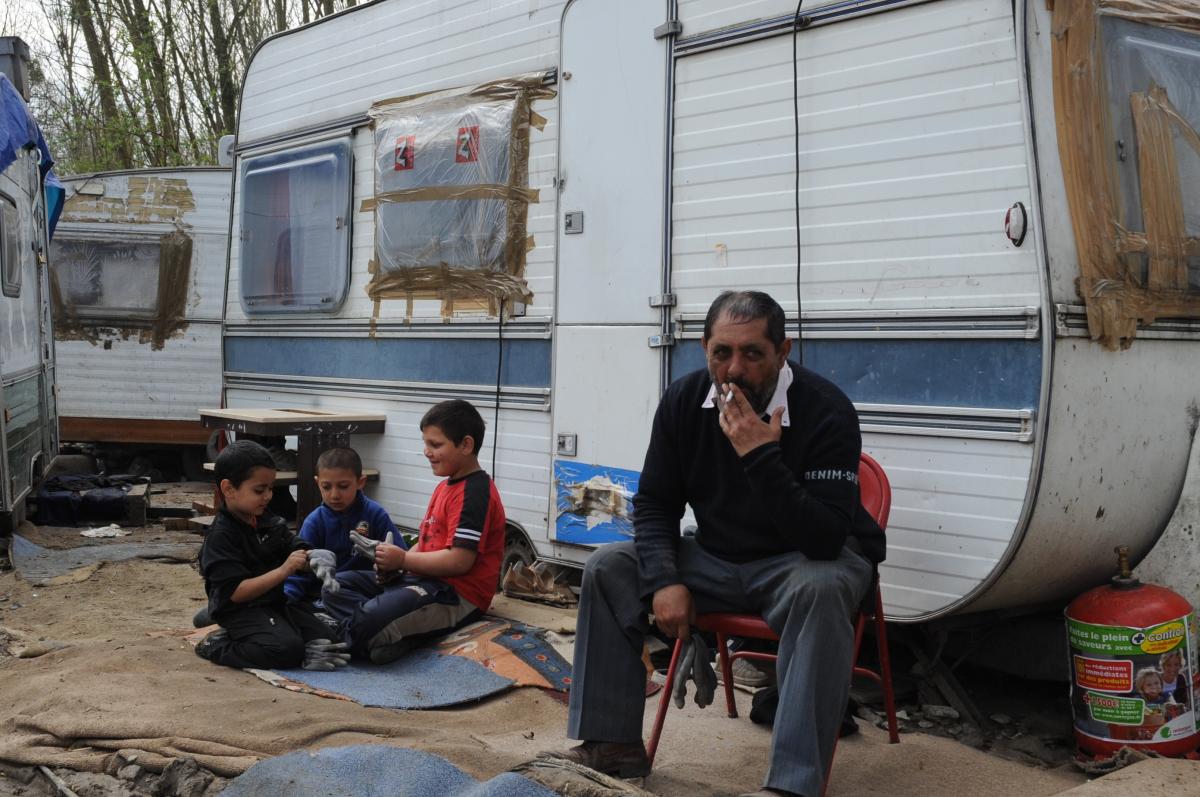 Adulte et enfants Roms devant leur vielle caravanne