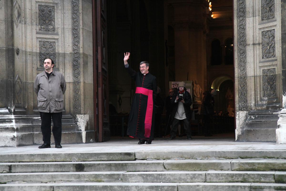 Le curé de l'église Saint François Xavier, dont les cloches sonnent à toutes volées, salue les manifestants