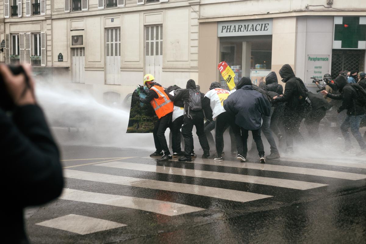 Des manifestants se protègent du canon à eau derrière une banderole