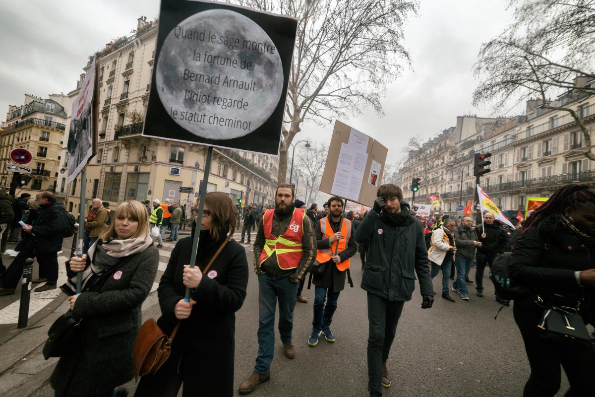 Une manifestante tient une pancarte Quand le sage montre la fortune de B Arnault, l'idiot regarde le statut cheminot