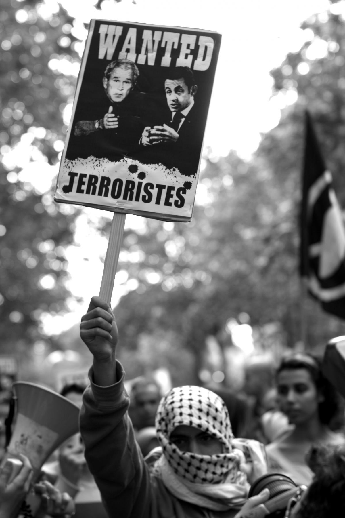 Militant avec foulard palestinien brandissant un panneau : Wanted terroristes Bush Sarkozy