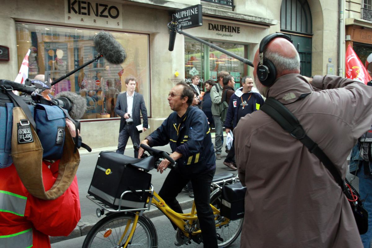 Facteur en vélo filmé par des journalistes.
