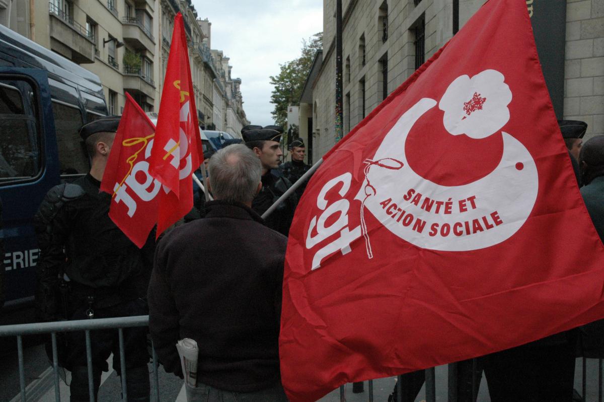 Manifestants CGT santé avec leurs drapeaux devant des CRS bloquant les accès au ministère du Travail.