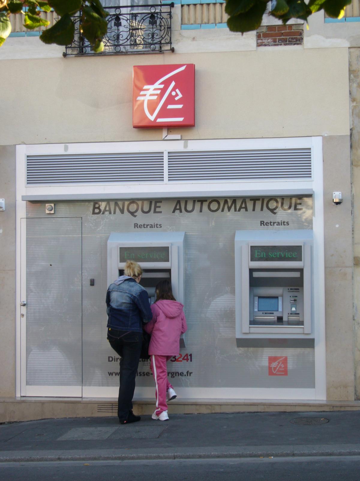 Un couple retire de l'argent au guichet automatique de la Caiss d'épargne.