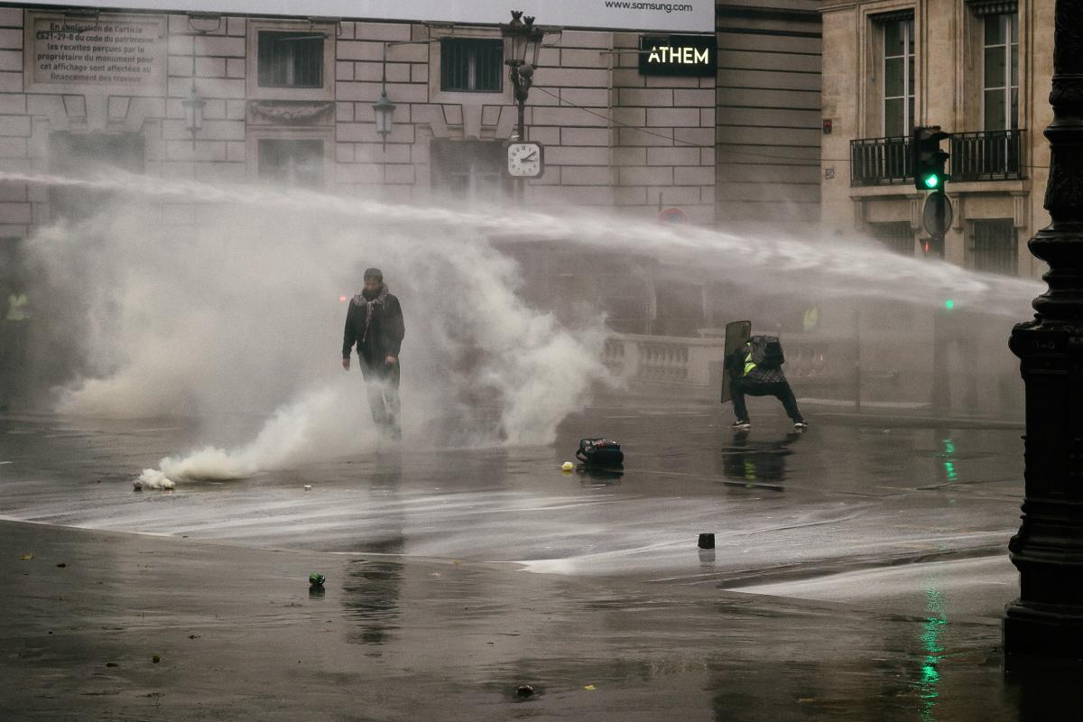 Un manifestant avec un bouvclier de la police face au canon à eau